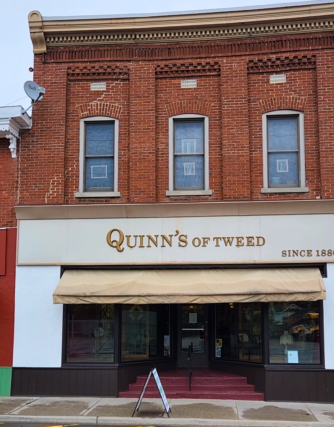 Quinn's of Tweed Storefront. A large red brick building with gold lettering that reads Quinn's of Tweed